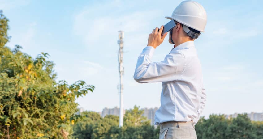 Wearing a white safety helmet, engineers study mobile phone signals (site survey for signal strength)