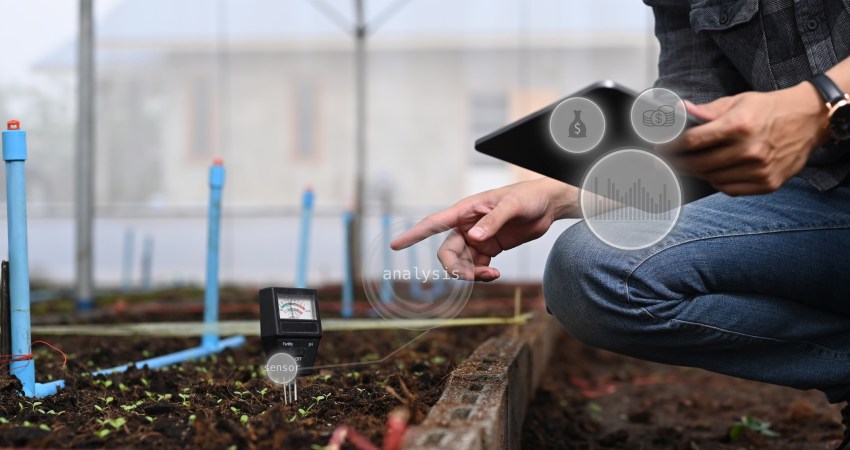 Soil Sensors: Close up view of agronomist using digital tablet for checking soil quality or pH value before seed plant in the greenhouse. Agriculture technology concept.